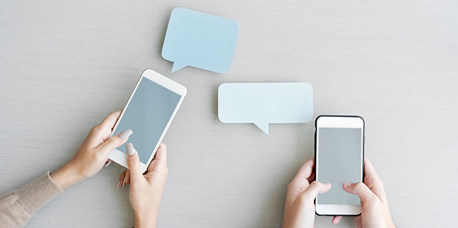 Two sets of hands holding mobile phones with two chat bubbles floating above them.