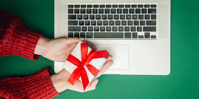 Laptop with hand holding a present wrapped in a red bow over keyboard green background
