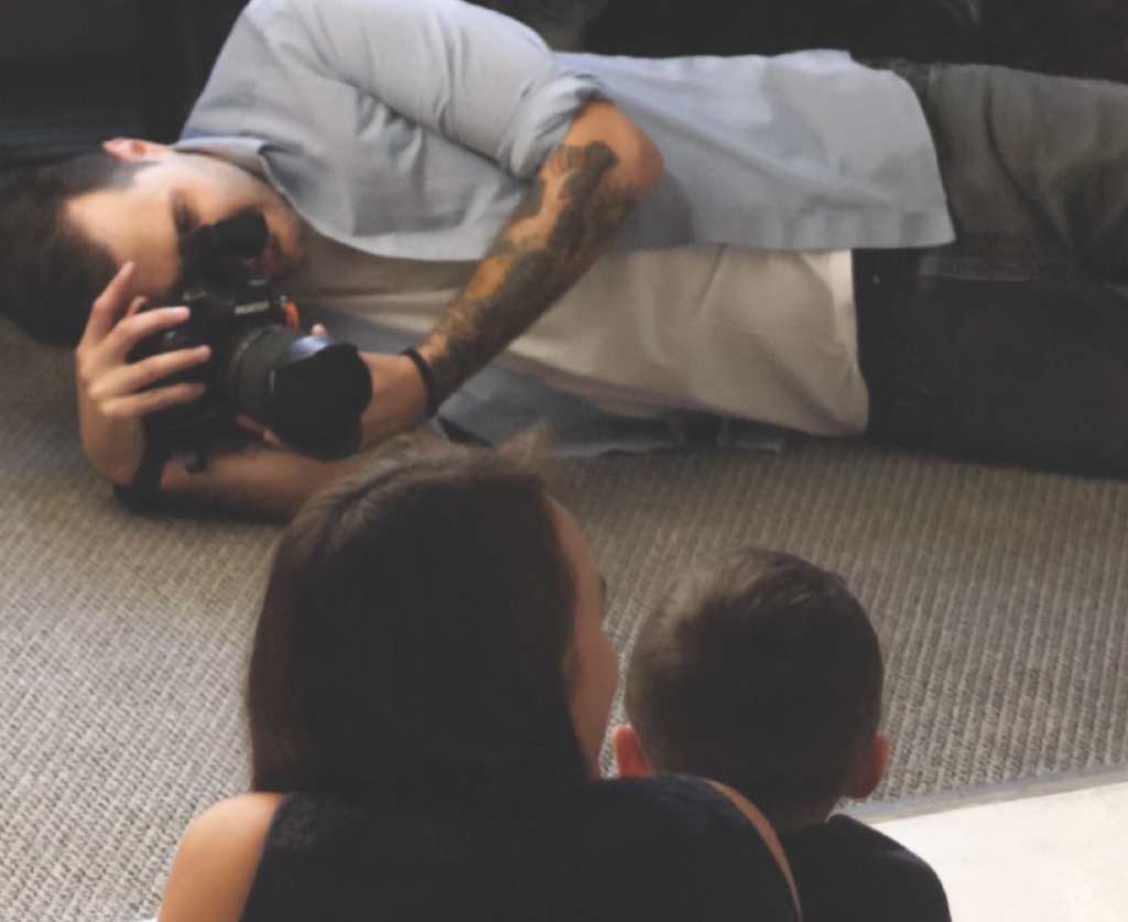 photographer lying on the floor taking a photo with a DSLR camera of a woman and her child